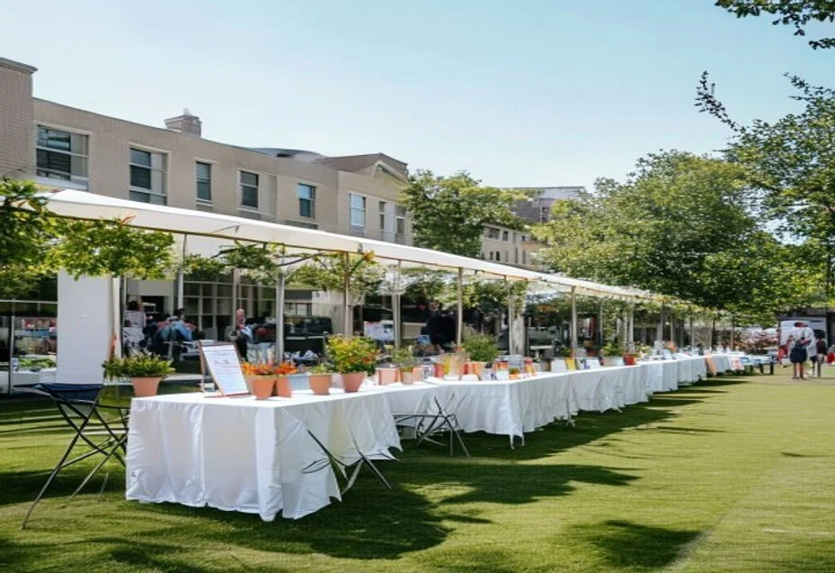 A long row of white marquee stalls with cloth-covered tables set up on a campus lawn
